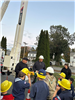 Two lineworkers explain safety to a group of cub scouts wearing yellow hard hats.