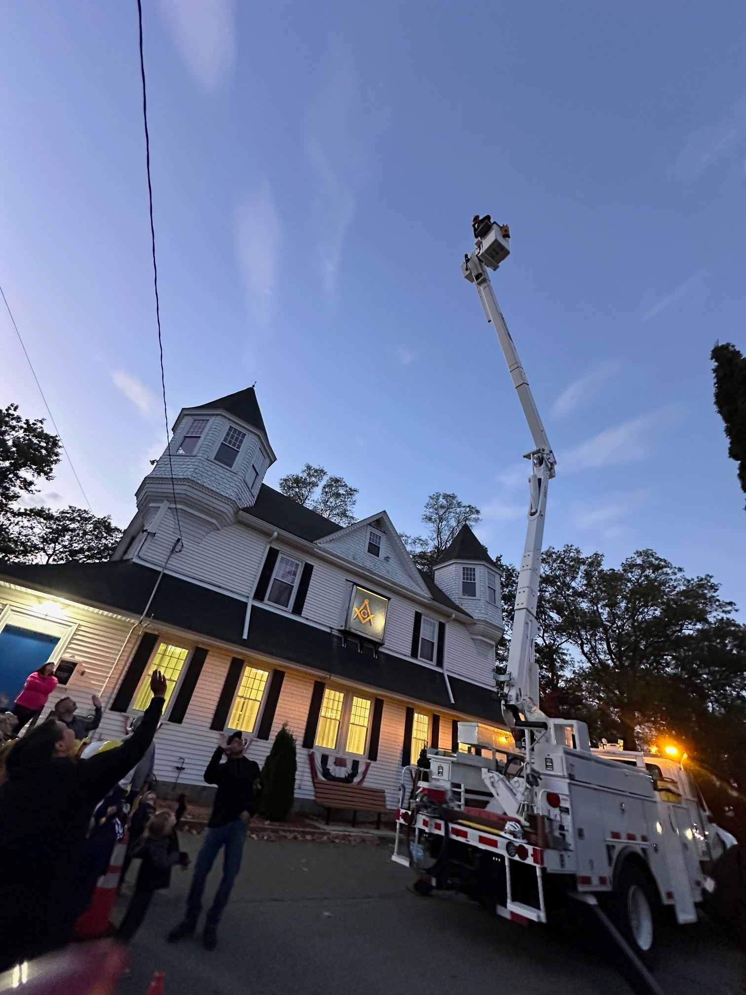 A lineworker at the top of a bucket truck with kids waving from below.