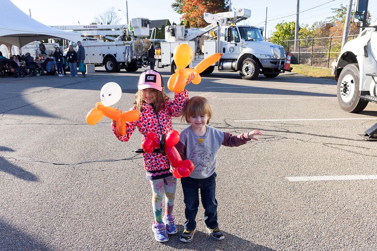 Two kids post with their balloon animals in front of bucket trucks at RMLD. 